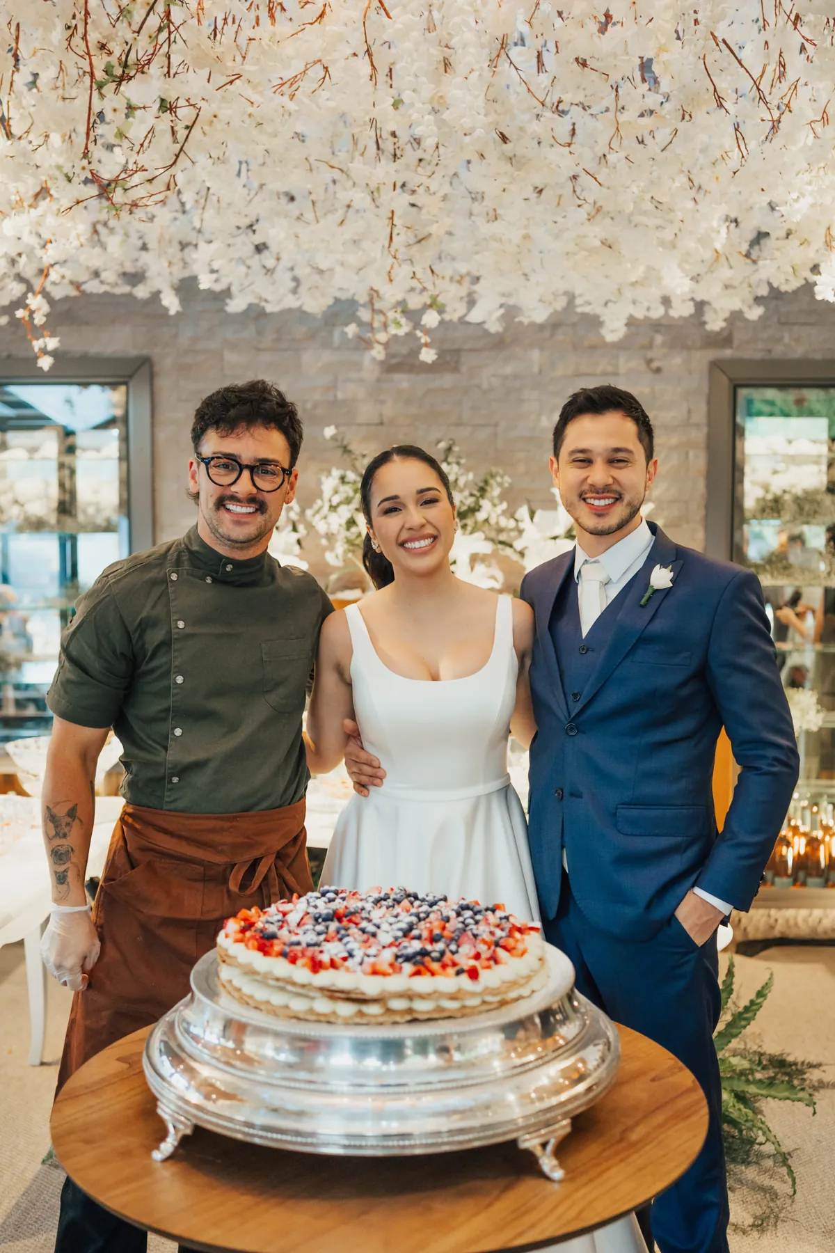 Bruno ao lado dos noivos e do bolo de frutas vermelhas