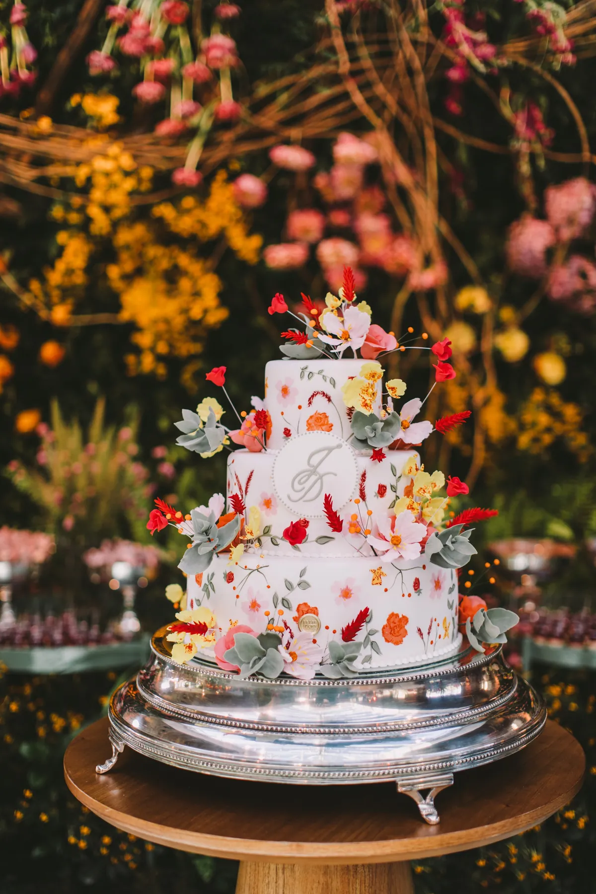 Bolo branco com flores coloridas, sobre bandeja de prata