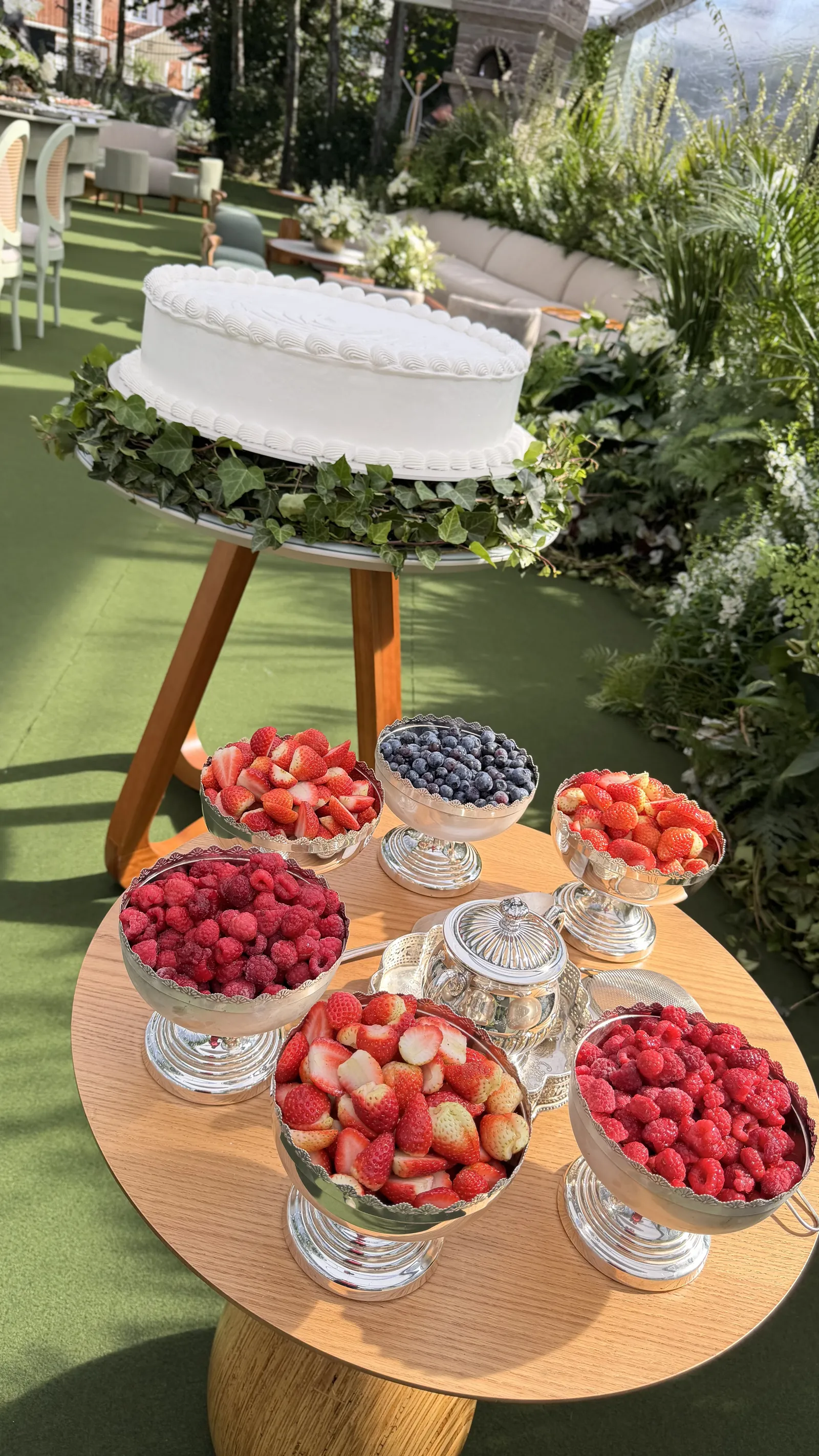 Bolo branco sobre suporte de madeira com taças de frutas vermelhas ao redor